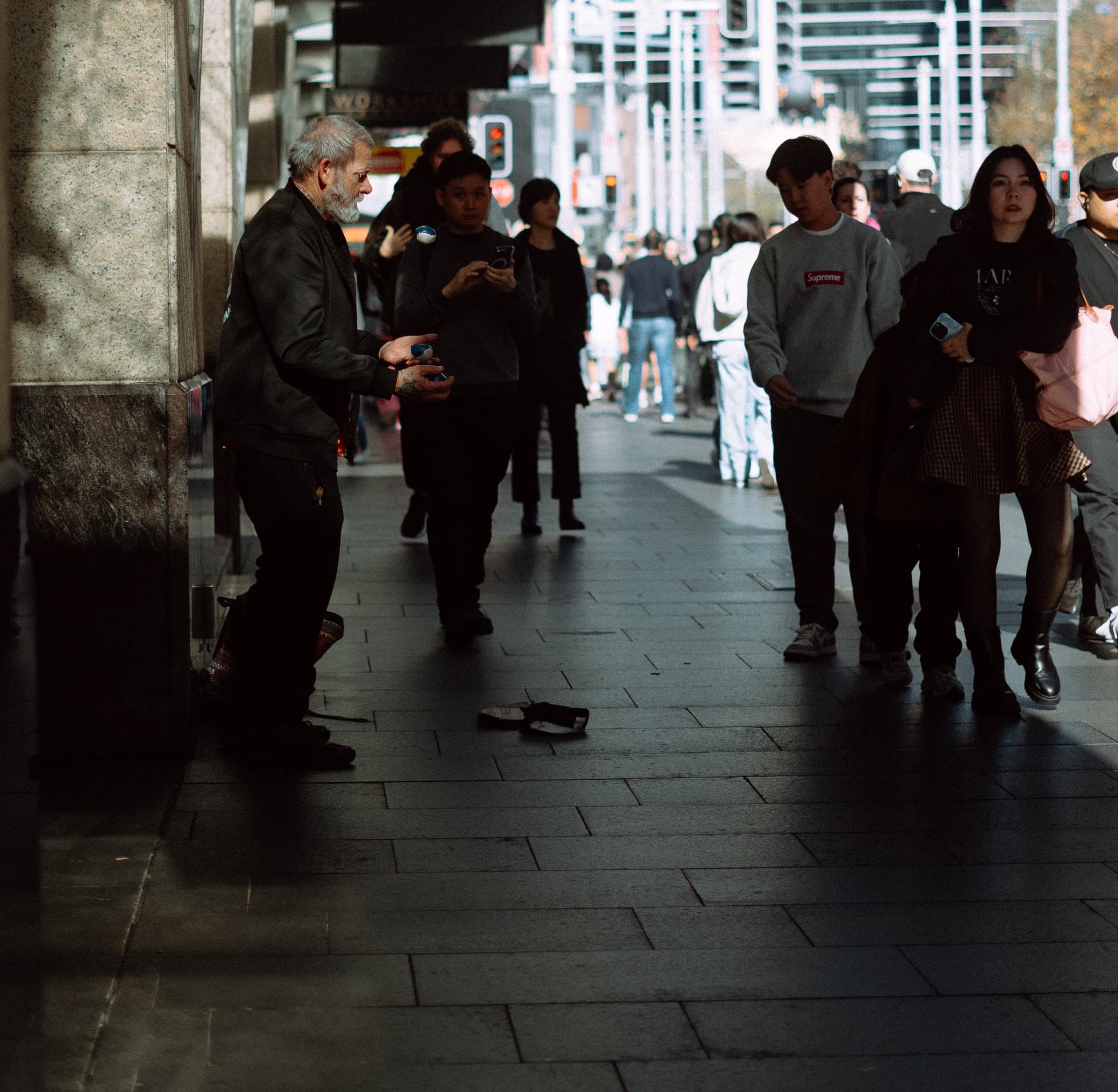 Street performer juggling in a pool of sunlight as shoppers stream past
