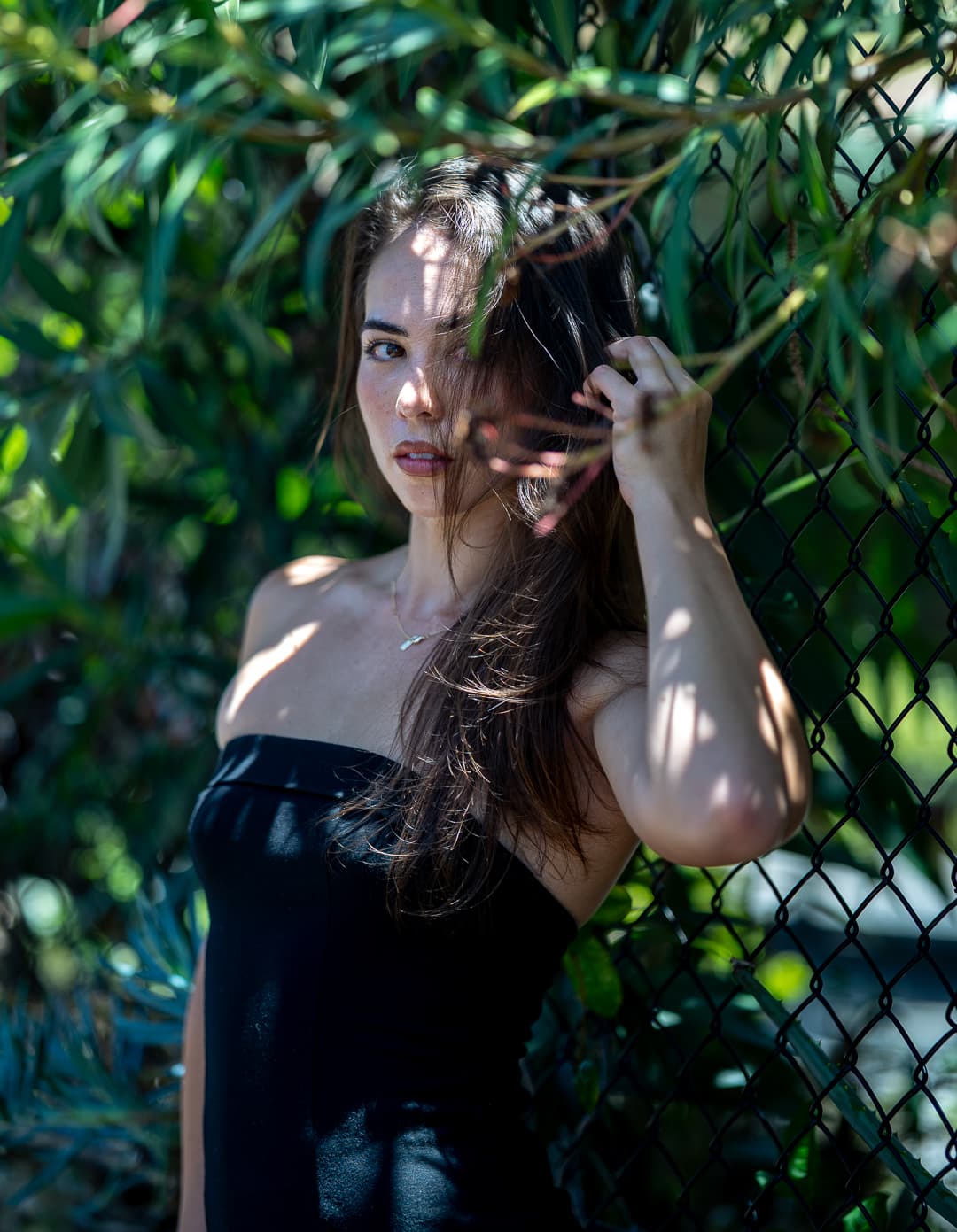 Woman in a black dress against a chain-link fence, framed by hanging eucalyptus leaves