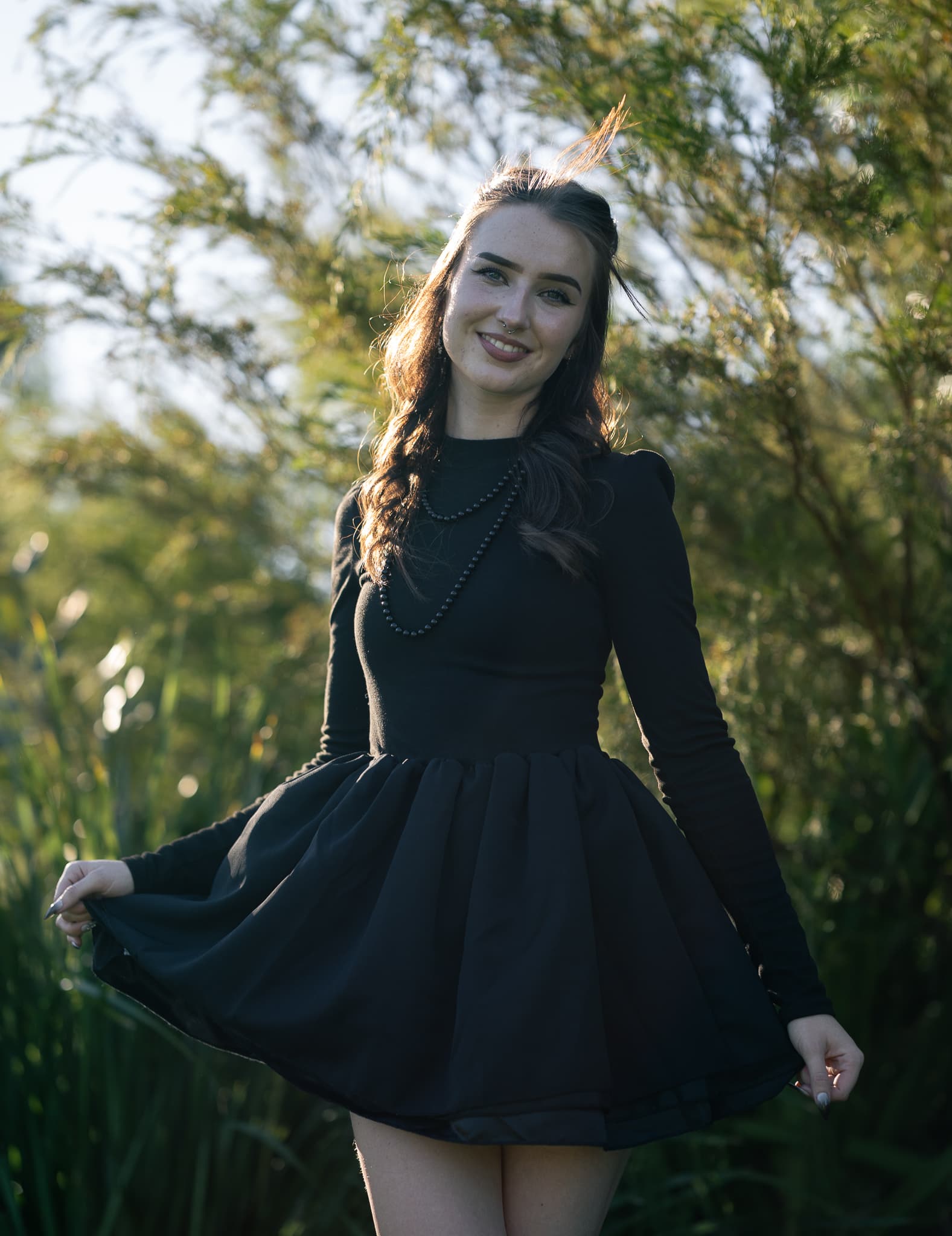 Smiling woman in a black dress fanning out her skirt in golden backlight