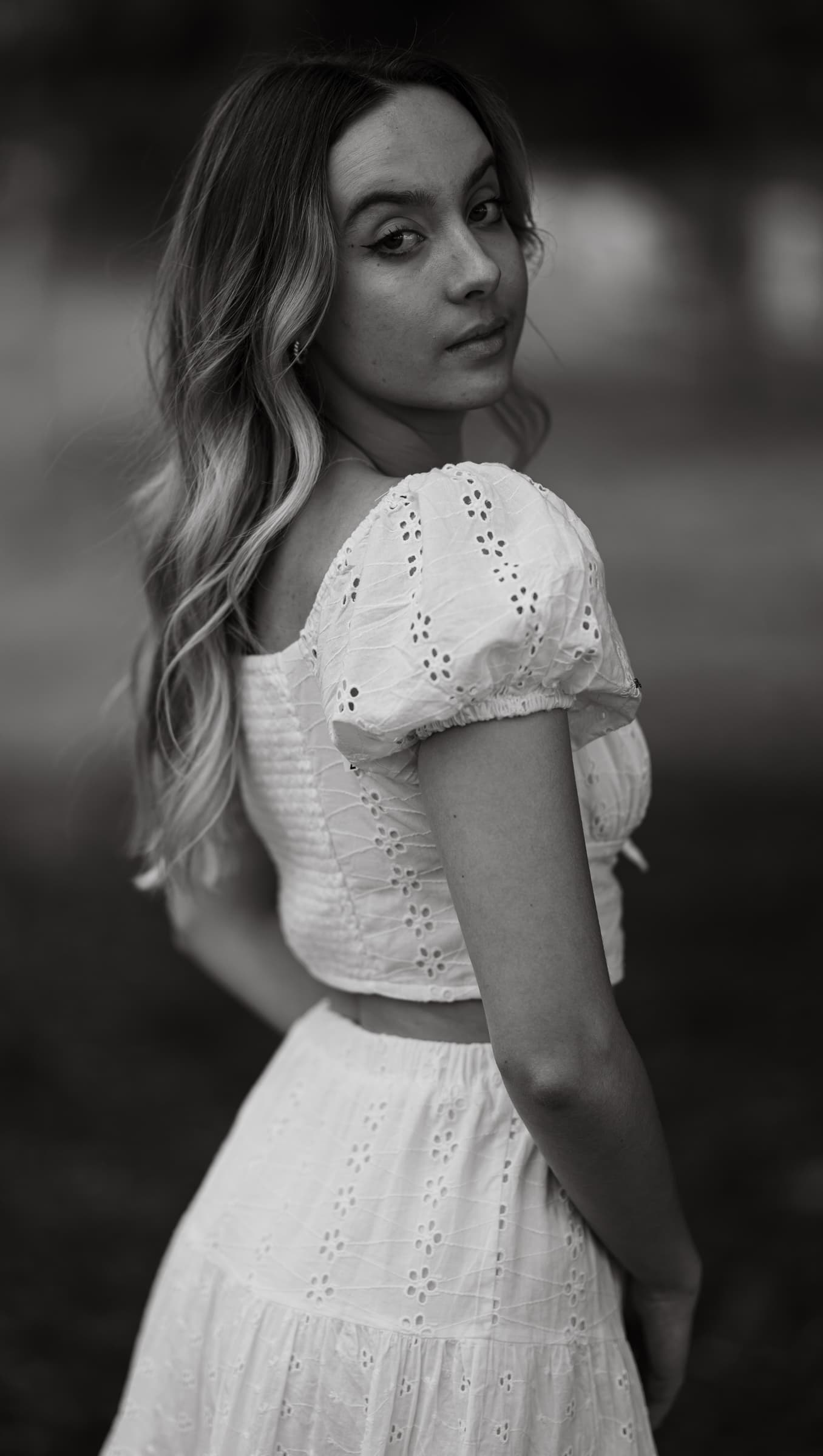 Black and white portrait of a woman in a white eyelet dress looking over her shoulder