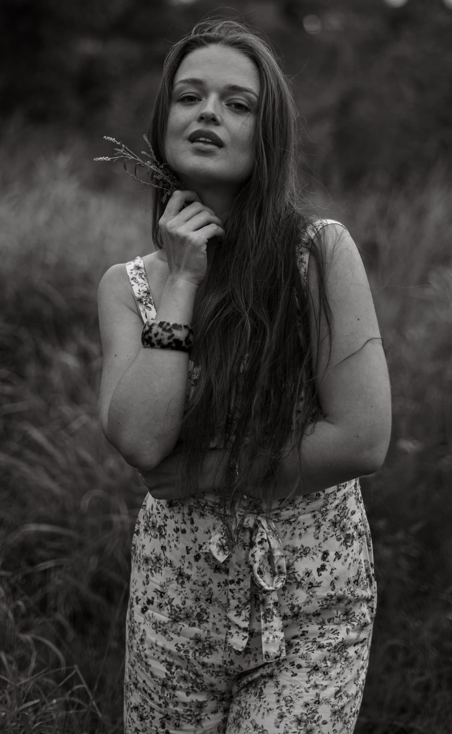 Black and white portrait of a woman in a floral jumpsuit holding a sprig of dried grass