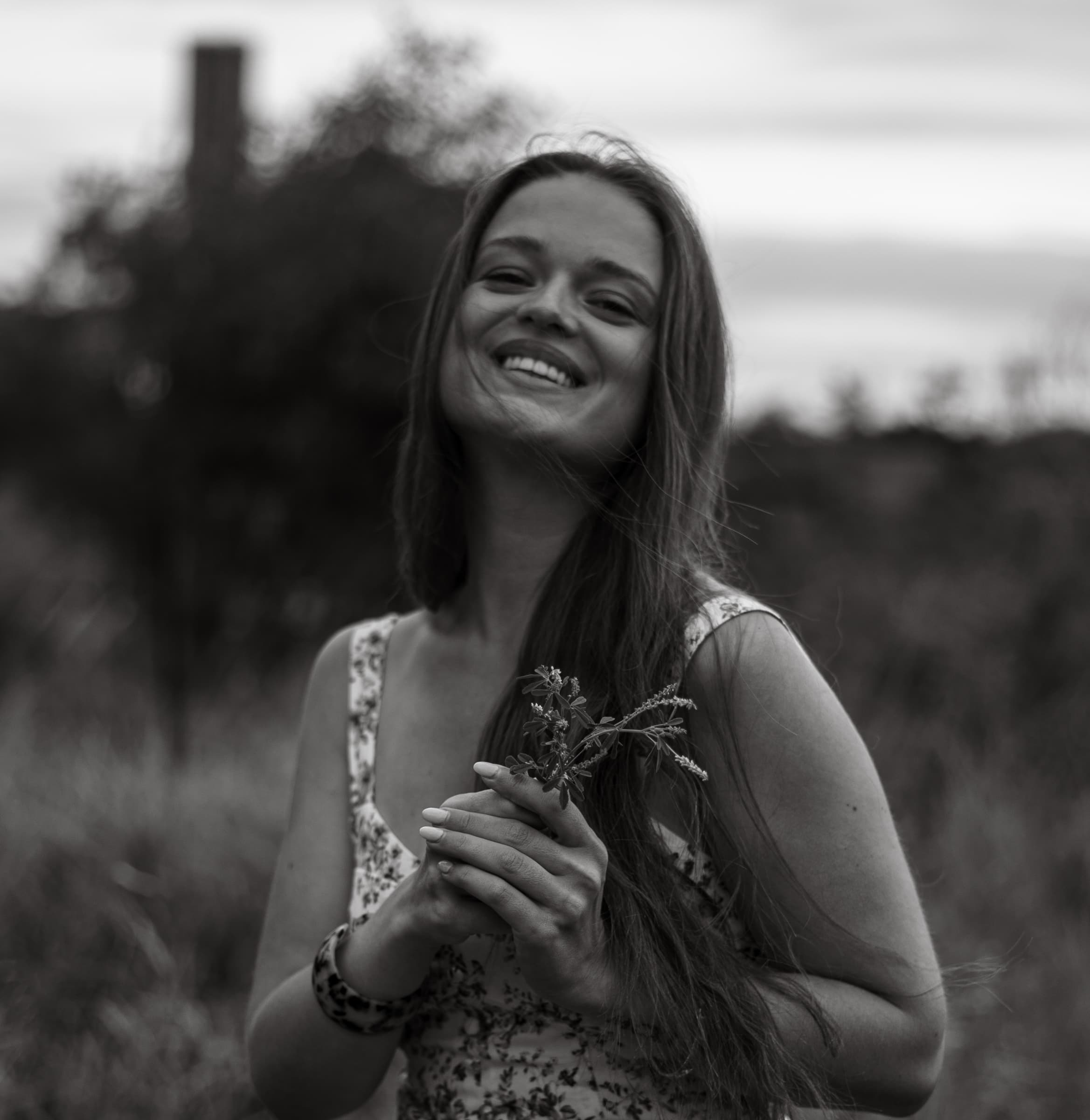 Black and white portrait of a laughing woman holding a small bunch of wildflowers