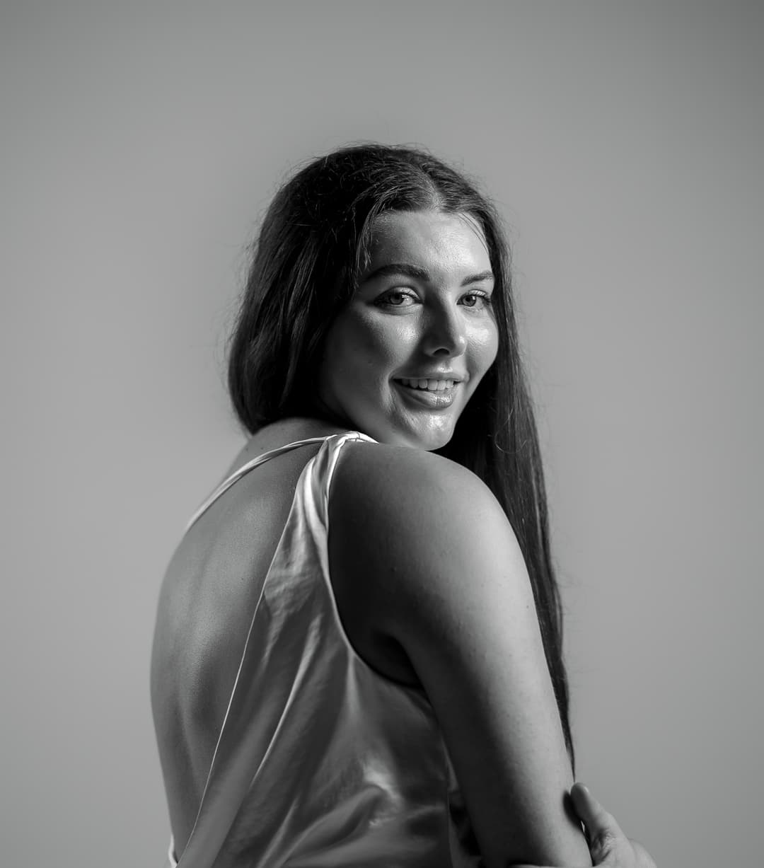 Black and white studio portrait of a woman in a satin top looking back over her shoulder