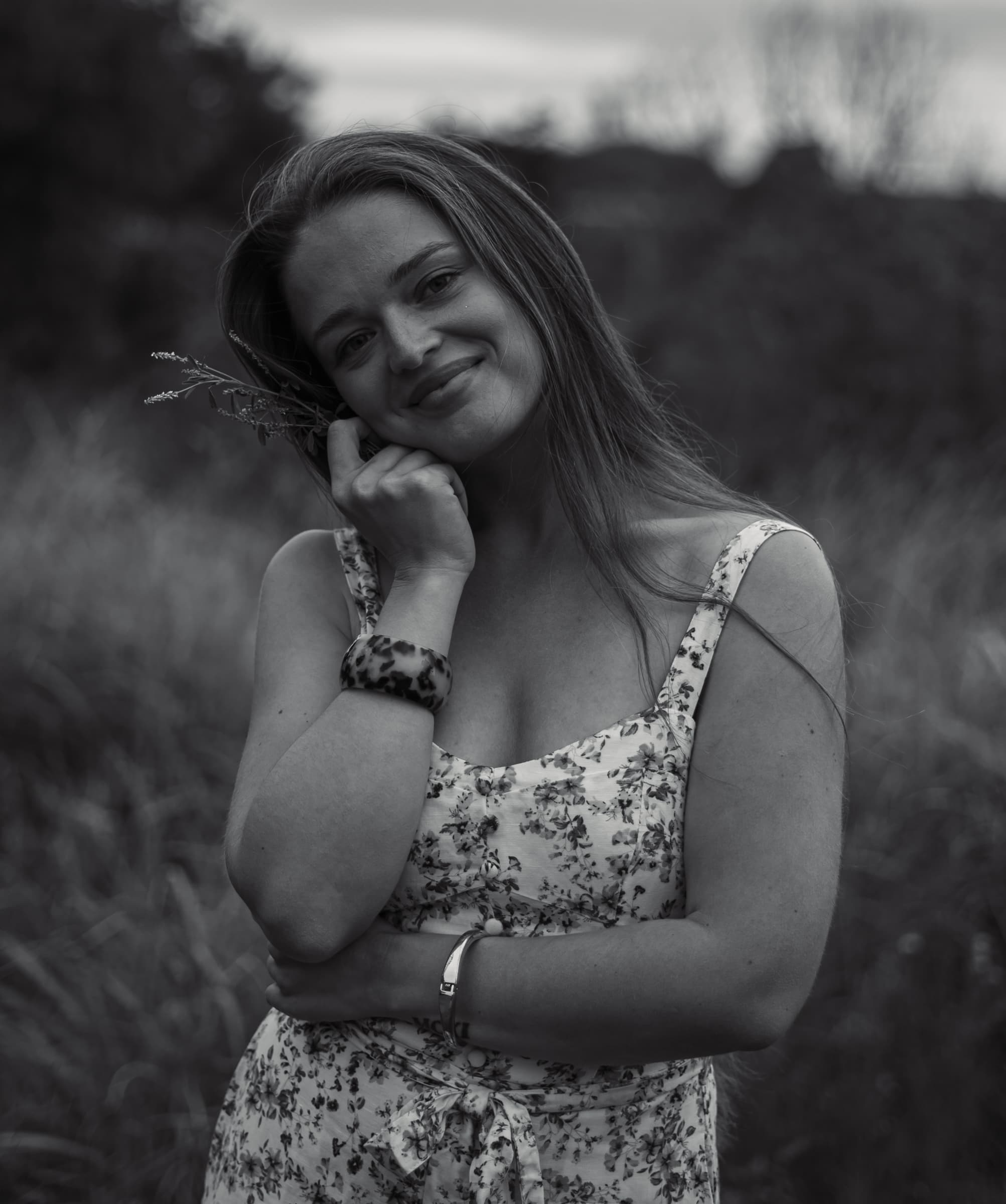Black and white portrait of a smiling woman holding wildflowers to her cheek in a field