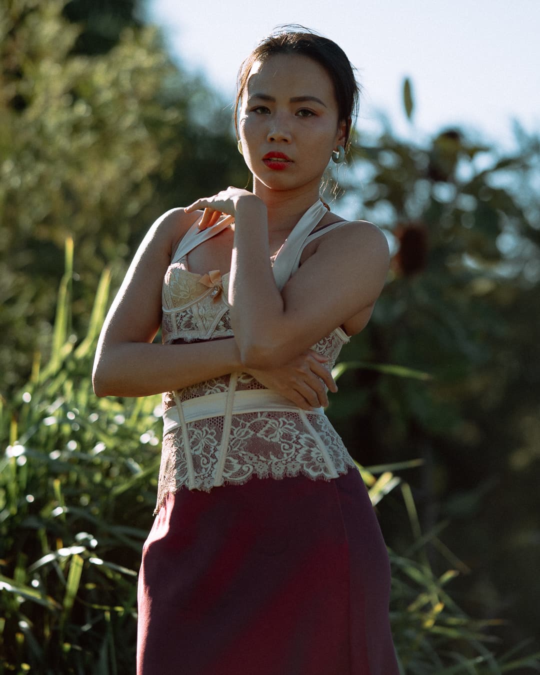 Woman in a lace top and deep red skirt standing among tall reeds in hard afternoon sun