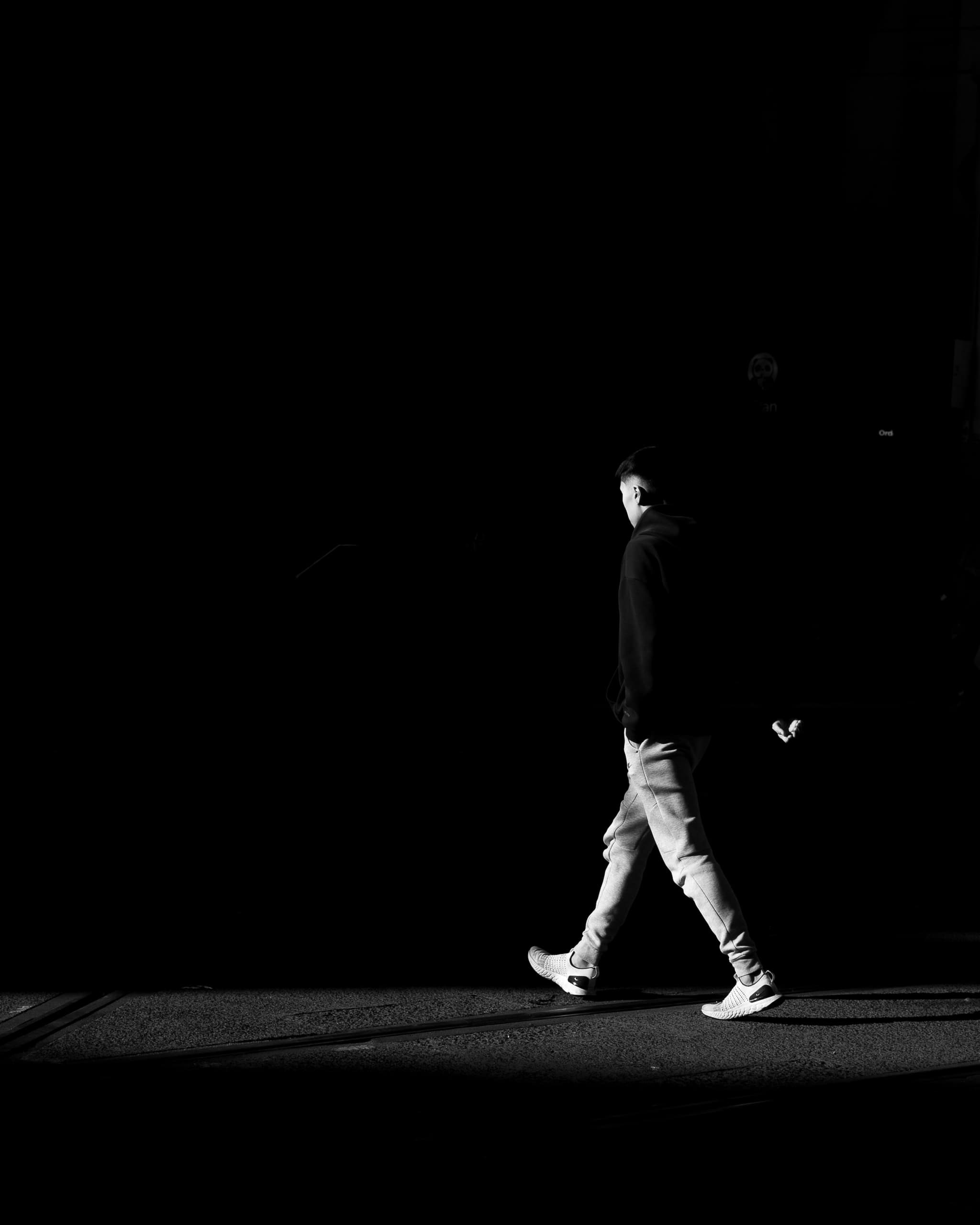 Black and white frame of a man in a hoodie walking through a blade of light