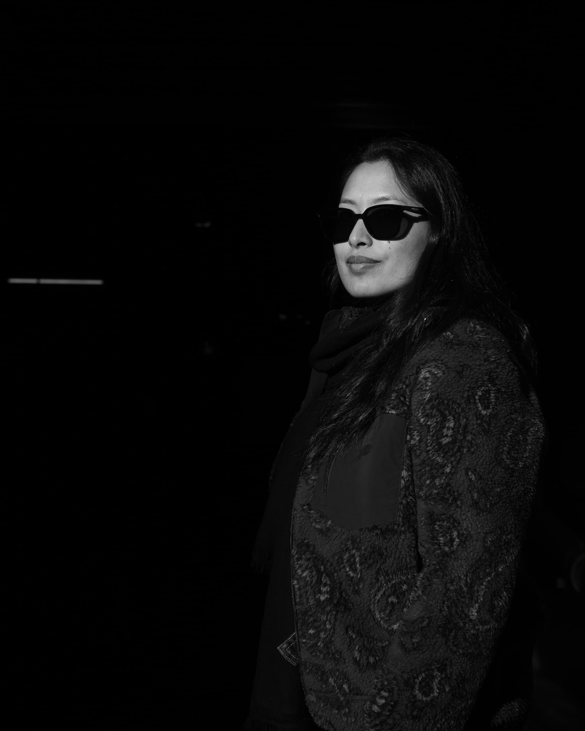 Black and white portrait of a woman in sunglasses and a fleece jacket in low sun