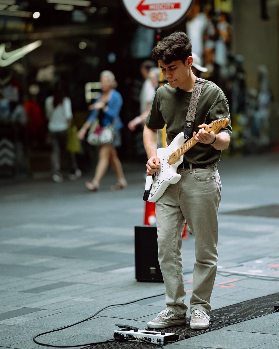 Teenage busker playing a white electric guitar in a shopping arcade