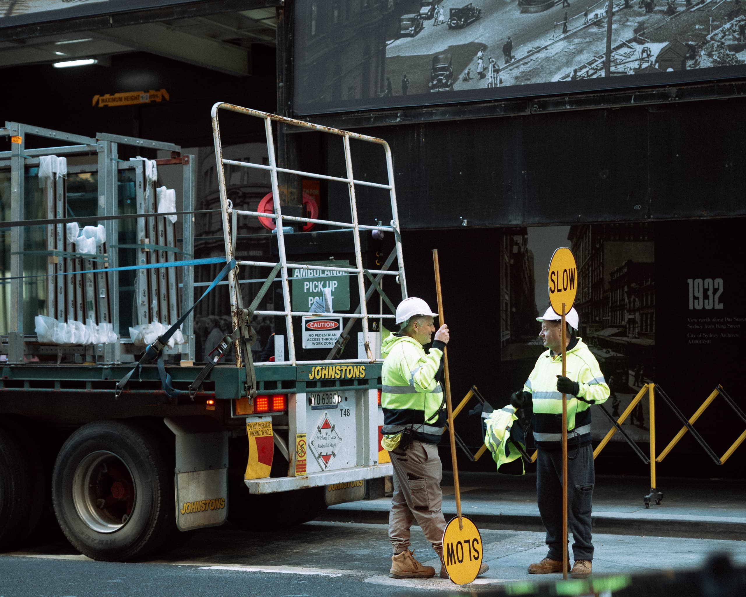 Two traffic controllers holding Slow signs, chatting behind a flatbed truck
