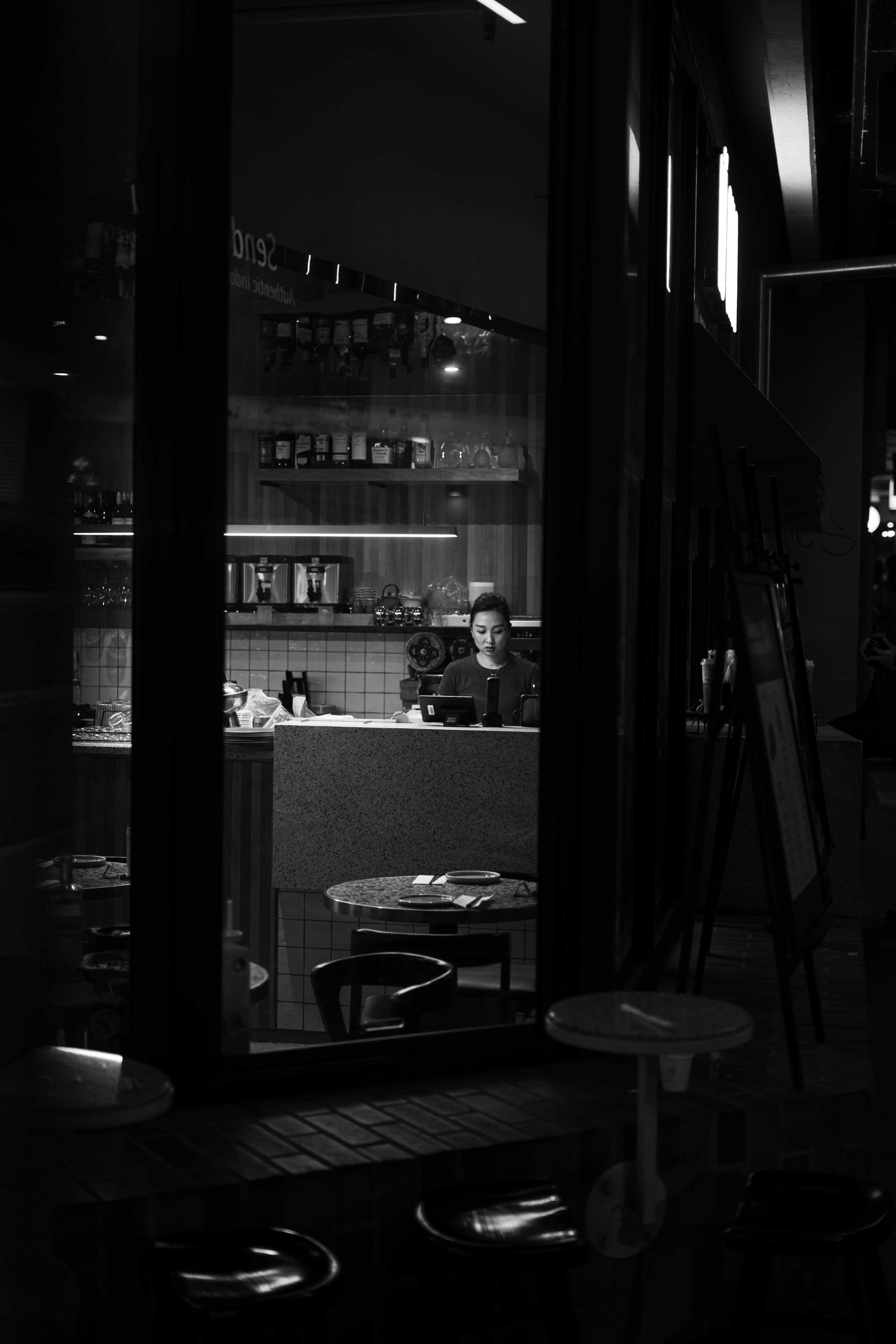 Black and white night view through a cafe window, a worker behind the lit counter