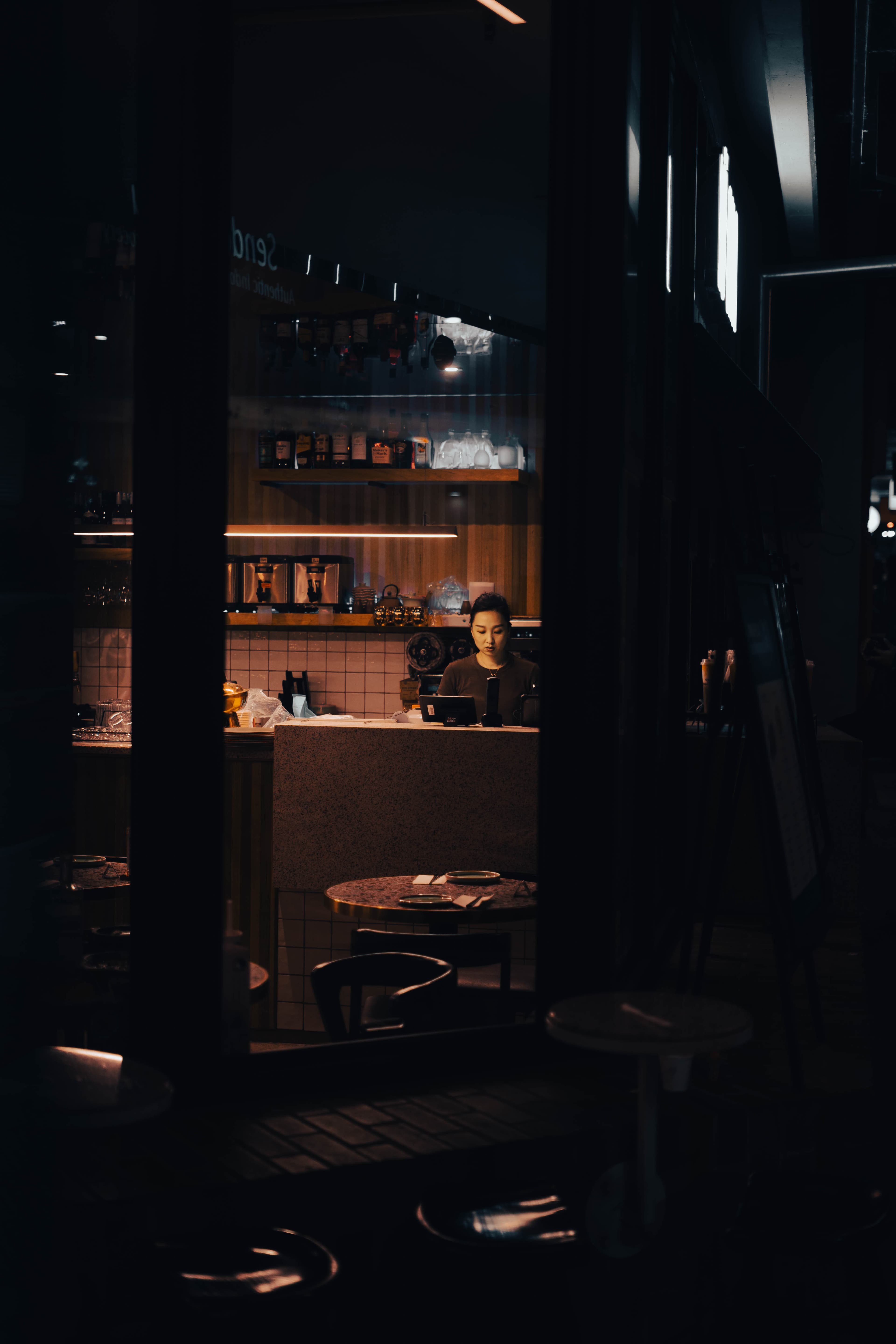 Barista behind a cafe counter framed by the doorway from the dark street
