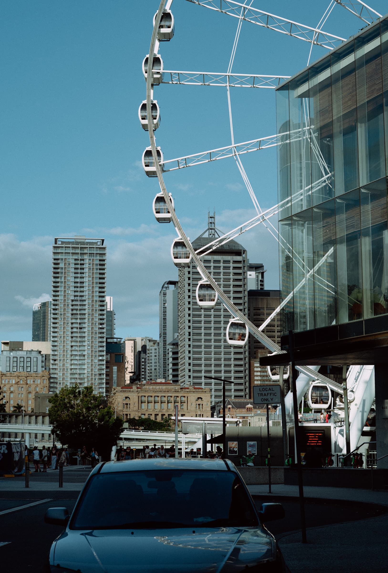 White ferris wheel rising between city towers above a parked car