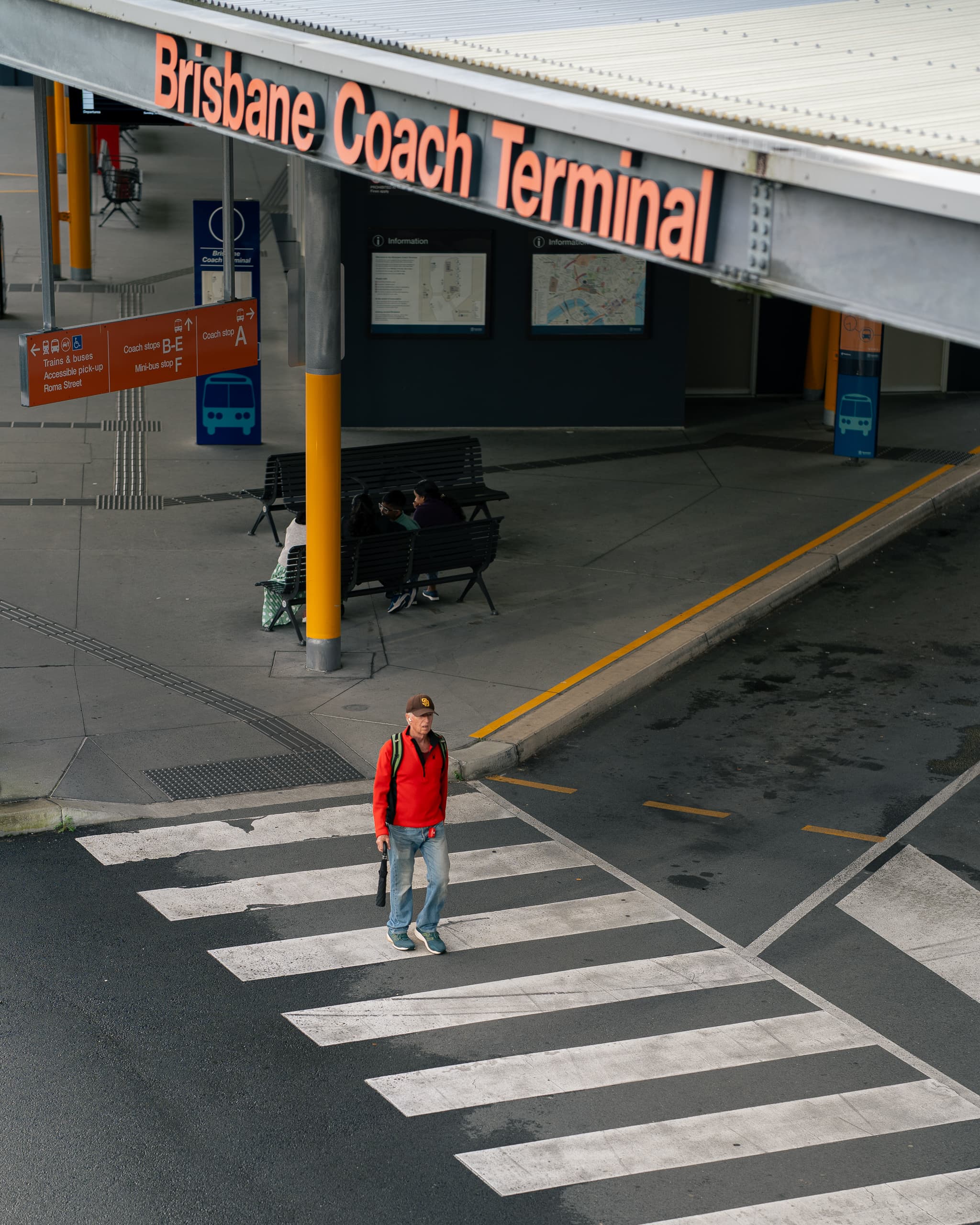 Man in a red jumper crossing the stripes at Brisbane Coach Terminal, seen from above