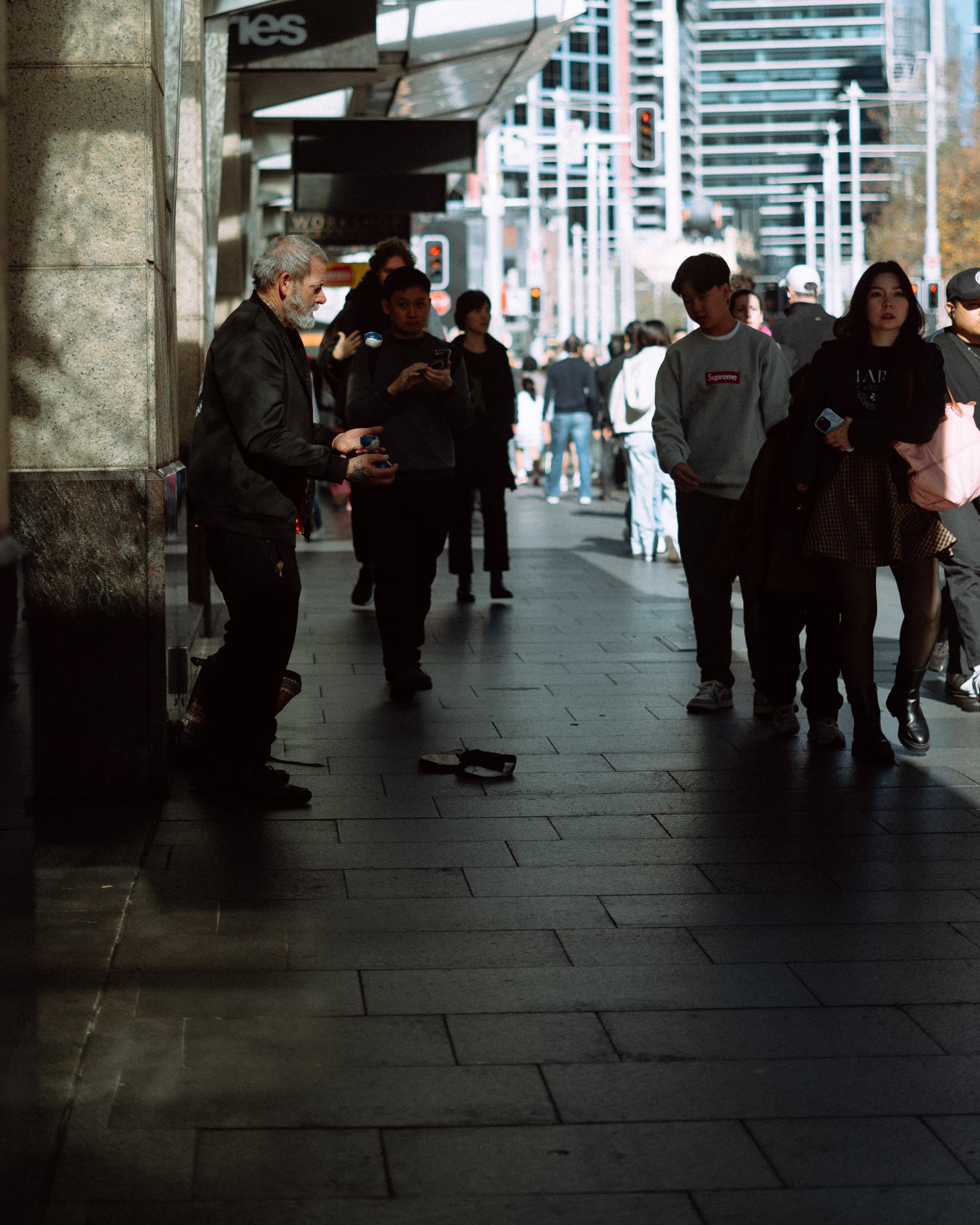 Street performer juggling in a pool of sunlight as shoppers stream past